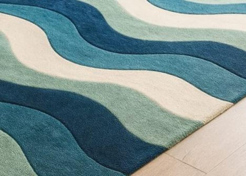 May include: A close-up of a rug with a wave pattern in shades of blue, teal, and off-white. The rug has a soft, textured appearance and is placed on a light-colored wooden floor.