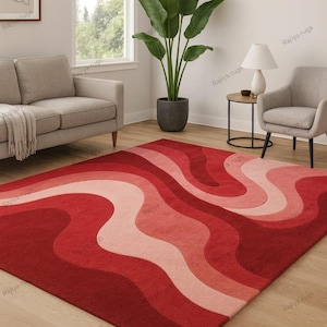 May include: A red area rug with a wavy pattern in shades of red and pink. The rug is rectangular and covers a wooden floor. The room also features a gray sofa, a chair, and a potted plant.