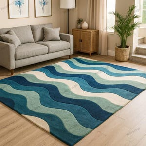 May include: A rectangular area rug with a wavy pattern in shades of blue and white. The rug features a textured design with alternating bands of dark blue, light blue, and off-white, creating a flowing, ocean-like appearance. The rug is placed on a wooden floor.