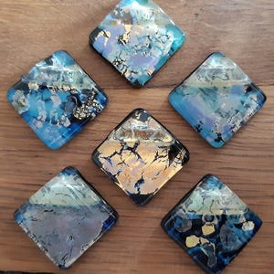 May include: Six diamond-shaped glass tiles with a blue, gold, and black abstract design. The tiles have a glossy finish and are perfect for adding a touch of color and texture to any space.