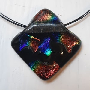 May include: A black glass pendant with iridescent rainbow colors, featuring a textured surface. The pendant is attached to a black cord.