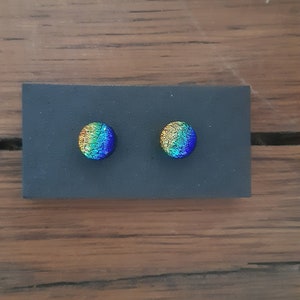 May include: A pair of round, iridescent glass earrings with a yellow, green, and blue color gradient. The earrings are displayed on a black background.