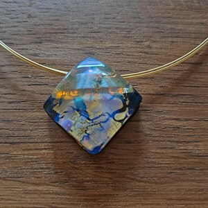 May include: A gold chain necklace with a diamond-shaped pendant. The pendant is made of clear glass with blue, gold, and purple swirls.