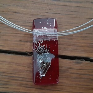 May include: A red glass pendant with a silver wire necklace. The pendant has a clear section with a piece of animal skin inside.