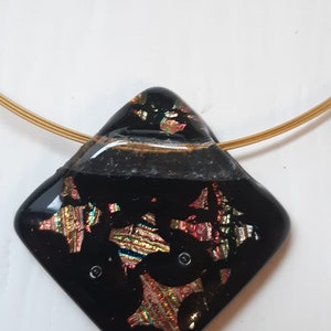 May include: A black glass pendant with gold and iridescent accents hangs from a gold chain. The pendant is shaped like a diamond and has a textured surface.