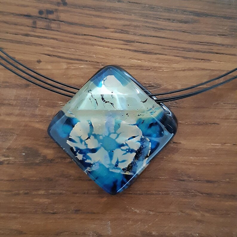 May include: A blue and white glass pendant with a black cord necklace. The pendant is a diamond shape with a swirling pattern.