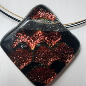 May include: A black and red glass pendant with a textured surface. The pendant is attached to a black and gold cord.