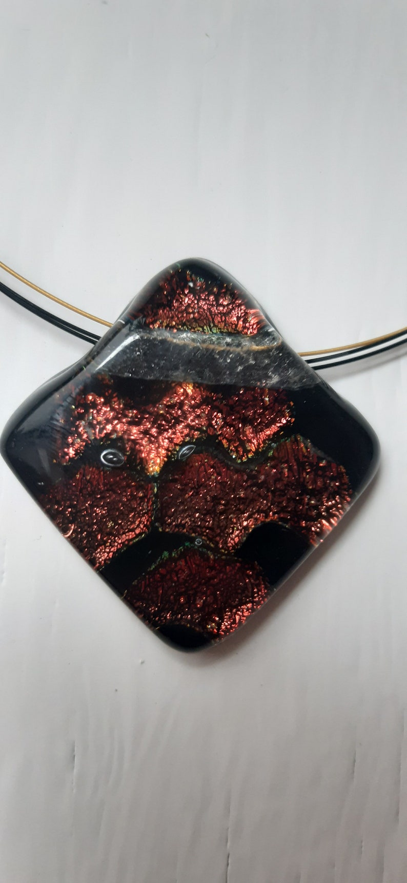 May include: A black and red glass pendant with a textured surface. The pendant is attached to a black and gold cord.