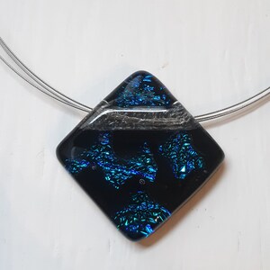 May include: A silver chain necklace with a square pendant made of black and blue dichroic glass. The pendant has a silver stripe across the center.