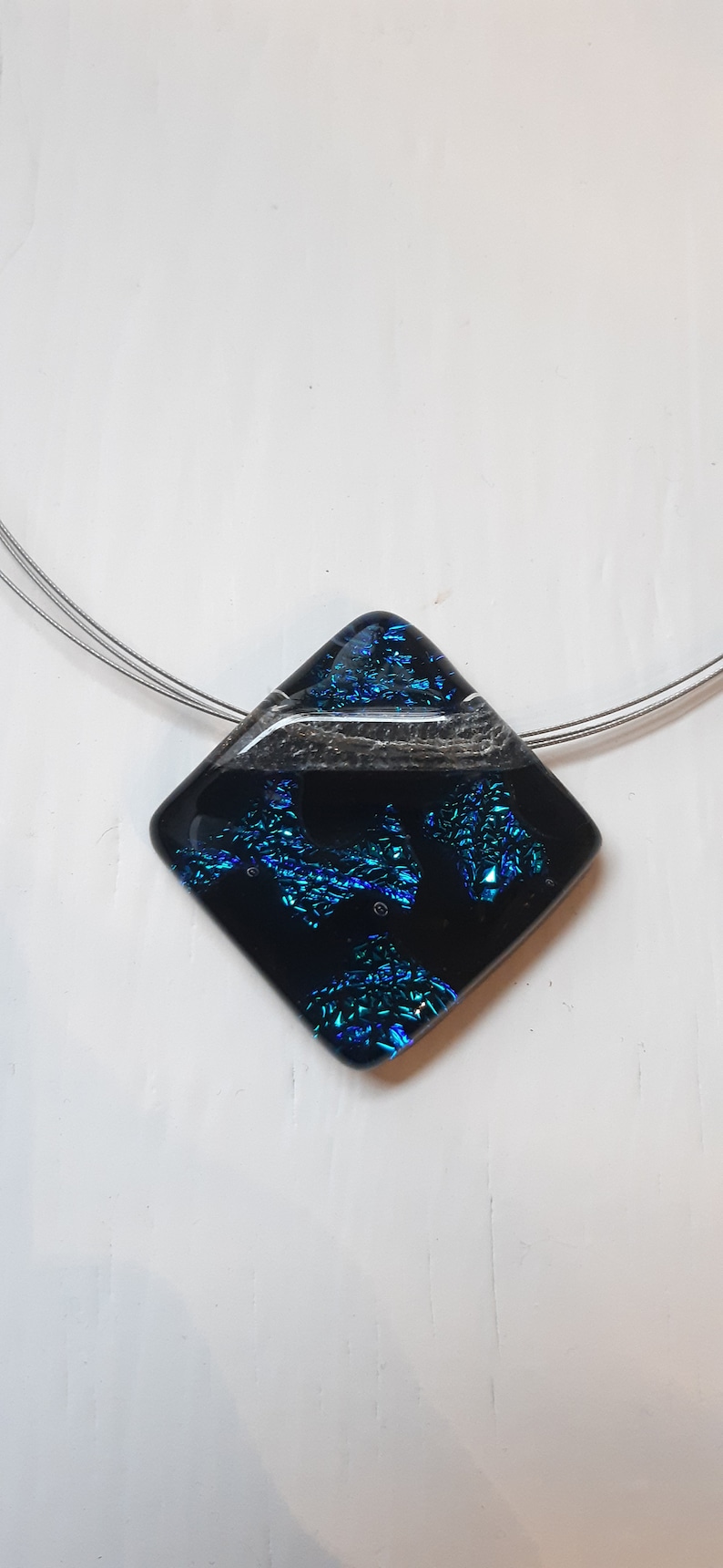 May include: A silver chain necklace with a square pendant made of black and blue dichroic glass. The pendant has a silver stripe across the center.