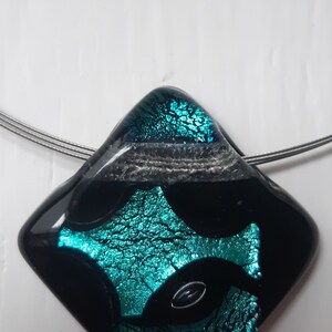 May include: A black and teal glass pendant with a diamond shape. The pendant has a silver wire attached to it.