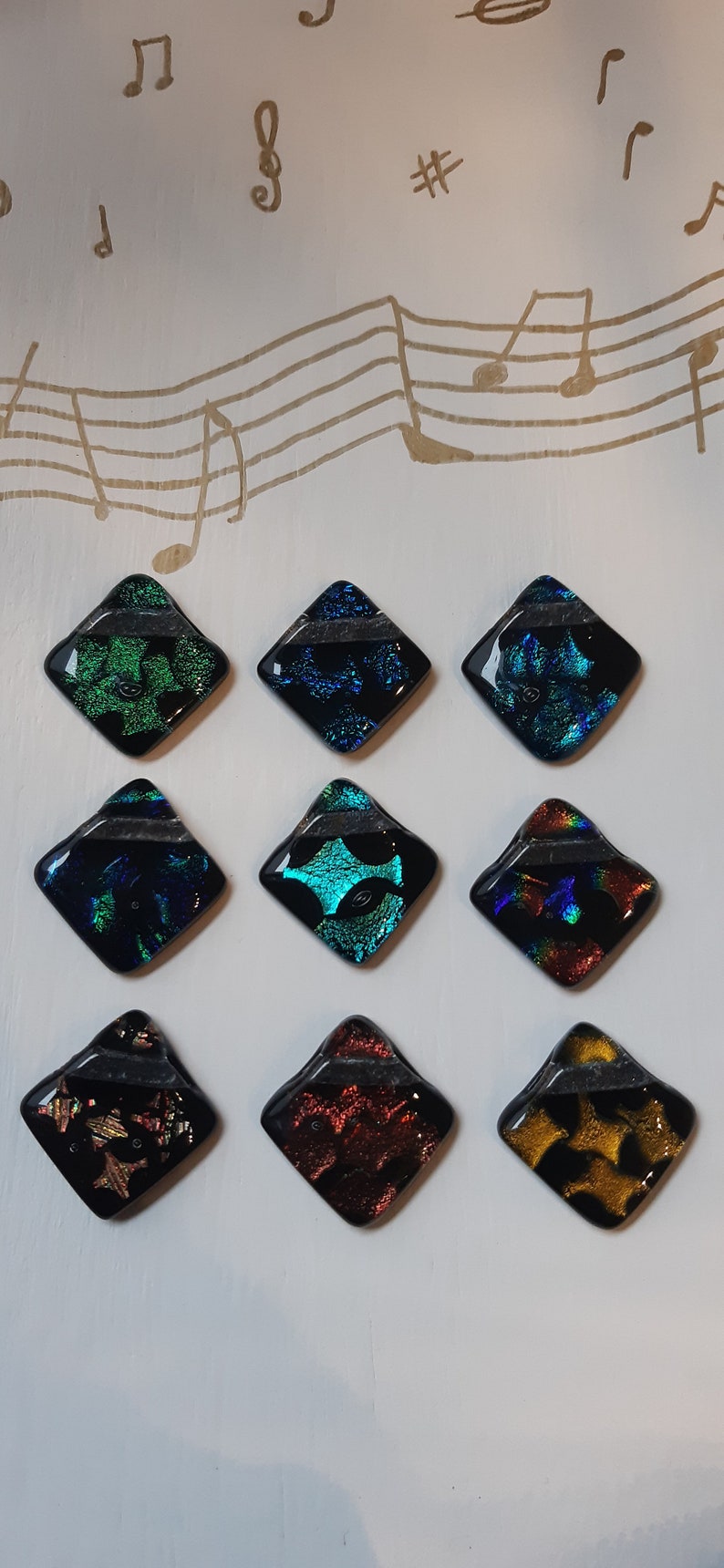 May include: Nine square-shaped glass tiles with iridescent finishes. The tiles are arranged in three rows of three. The tiles feature a variety of colors and patterns, including green, blue, red, and gold.