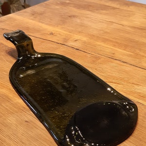 May include: A dark green glass bottle that has been repurposed into a serving tray. The tray has a handle and a slightly curved shape.