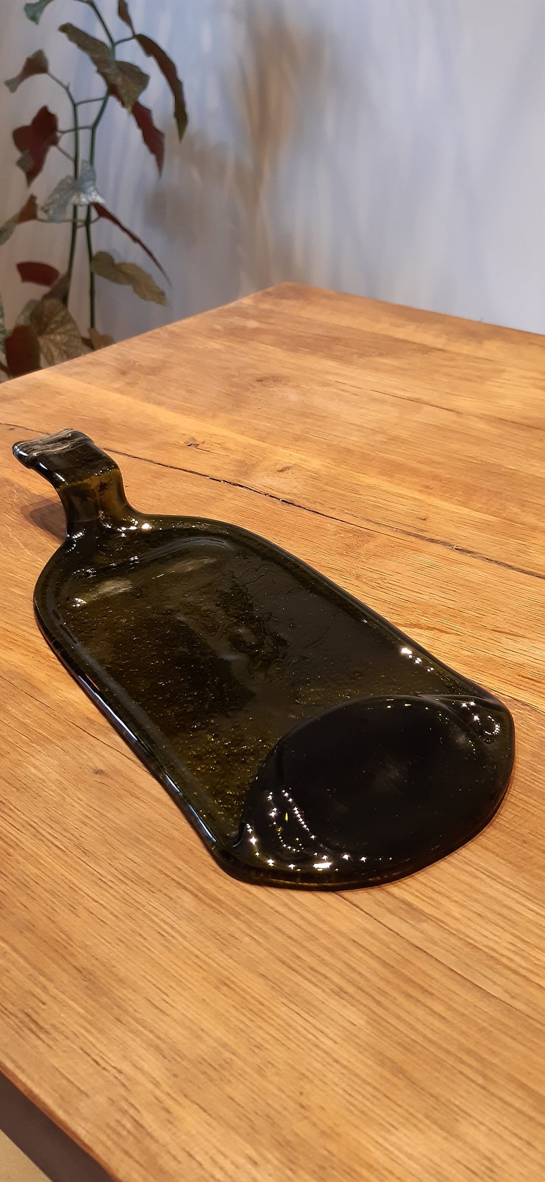 May include: A dark green glass bottle that has been repurposed into a serving tray. The tray has a handle and a slightly curved shape.