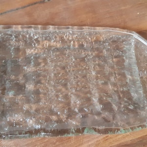 May include: A clear glass bottle that has been repurposed into a serving tray. The bottle has a textured surface and a handle on one end.