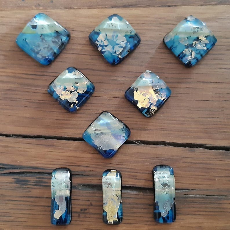 May include: Nine blue and gold glass tiles in diamond and rectangular shapes. The tiles have a marbled effect with gold flecks.