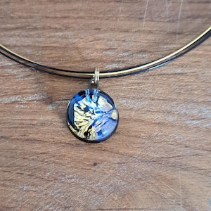 Puede incluir: Un collar de cadena dorada con un colgante redondo con un dise&ntilde;o abstracto azul y dorado.