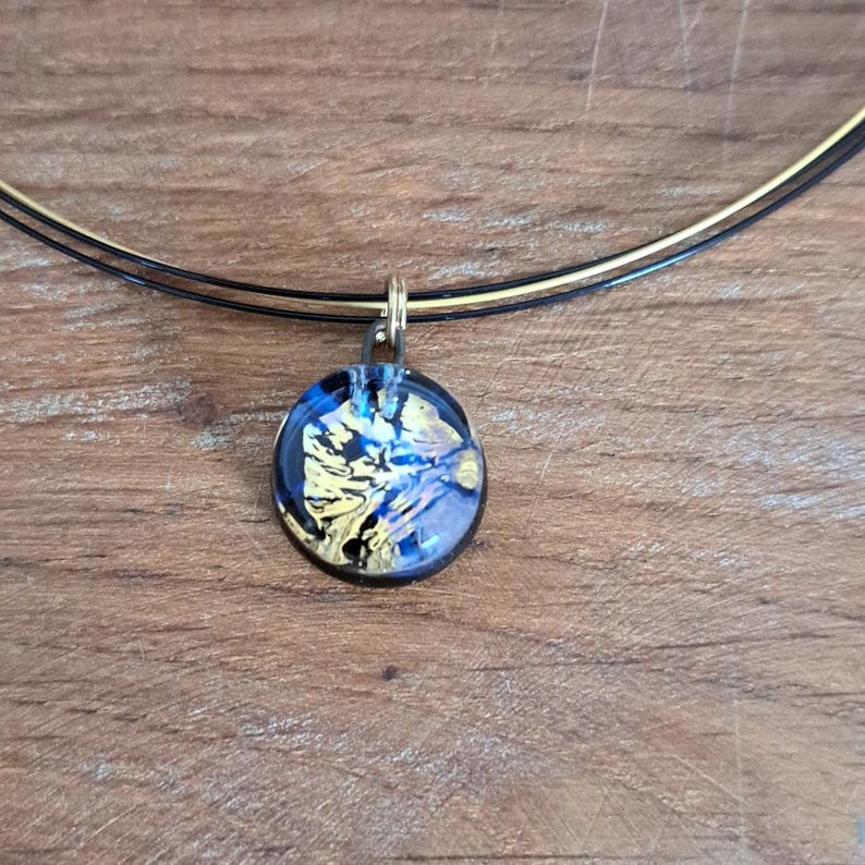 Puede incluir: Un collar de cadena dorada con un colgante redondo con un dise&ntilde;o abstracto azul y dorado.