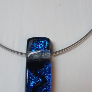K&ouml;nnte beinhalten: Eine silberne Kettenkette mit einem blauen und schwarzen Glasanh&auml;nger. Der Anh&auml;nger hat einen wei&szlig;en Streifen und eine glitzernde blaue Oberfl&auml;che.