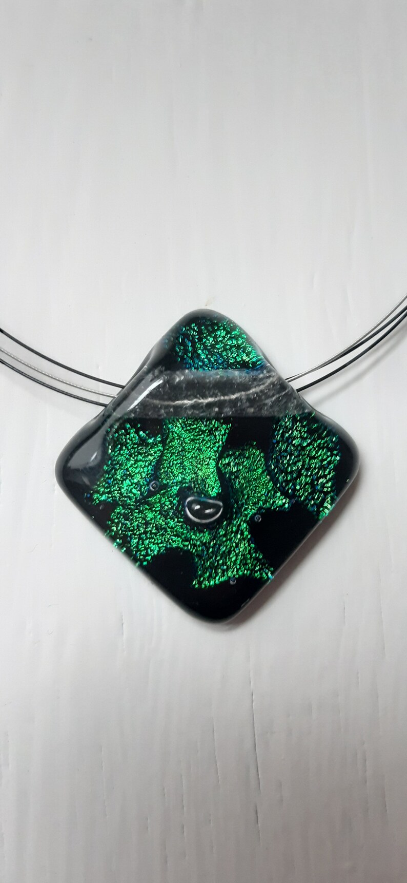 May include: A black and green glass pendant with a diamond shape and iridescent finish. The pendant is on a silver chain.