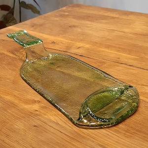 May include: A green glass bottle shaped serving tray with a handle. The tray is on a wooden surface.
