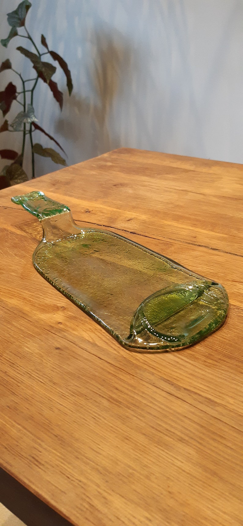 May include: A green glass bottle shaped serving tray with a handle. The tray is on a wooden surface.