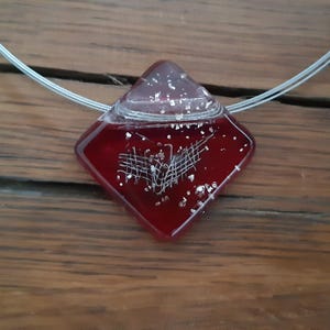 May include: A red glass pendant with a white design inside. The pendant is shaped like a diamond and is hanging from a silver chain.