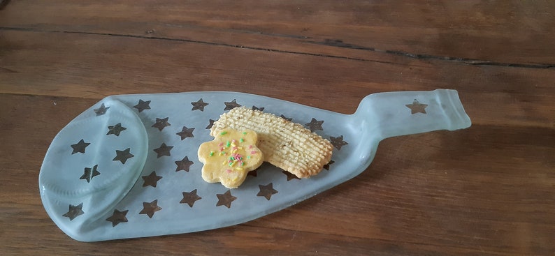 May include: A light blue glass serving tray shaped like a bottle with a star pattern. Two cookies are on the tray, one is a plain cookie and the other is a star-shaped cookie with sprinkles.