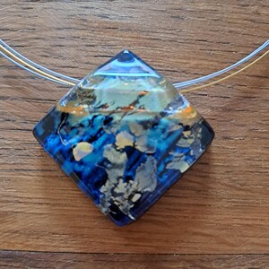 May include: A blue and gold glass pendant with a diamond shape. The pendant has a swirling pattern of blue, gold, and white.