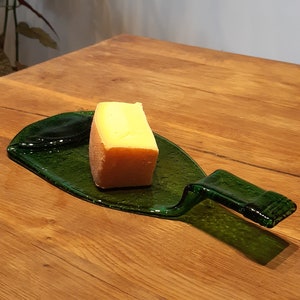 May include: A green glass bottle shaped into a serving tray with a block of cheese on top. The tray is sitting on a wooden table.