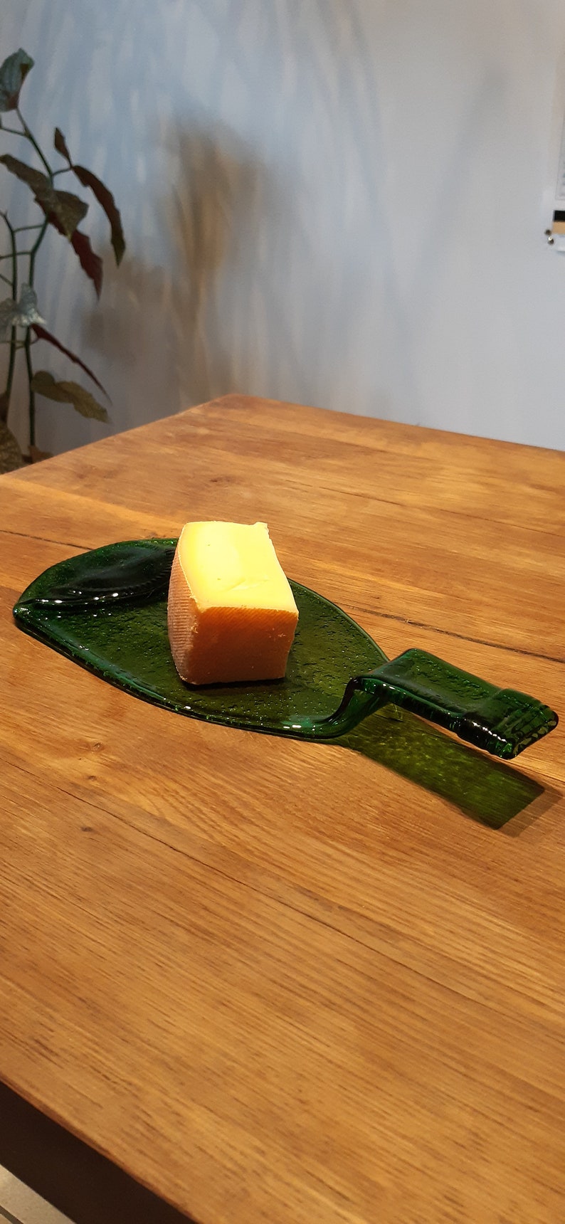 May include: A green glass bottle shaped into a serving tray with a block of cheese on top. The tray is sitting on a wooden table.