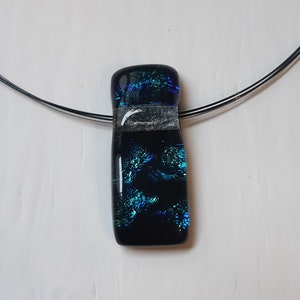 K&ouml;nnte beinhalten: Ein schwarzer Glasanh&auml;nger mit einem blauen und gr&uuml;nen, schillernden Muster h&auml;ngt an einer silbernen Kette.