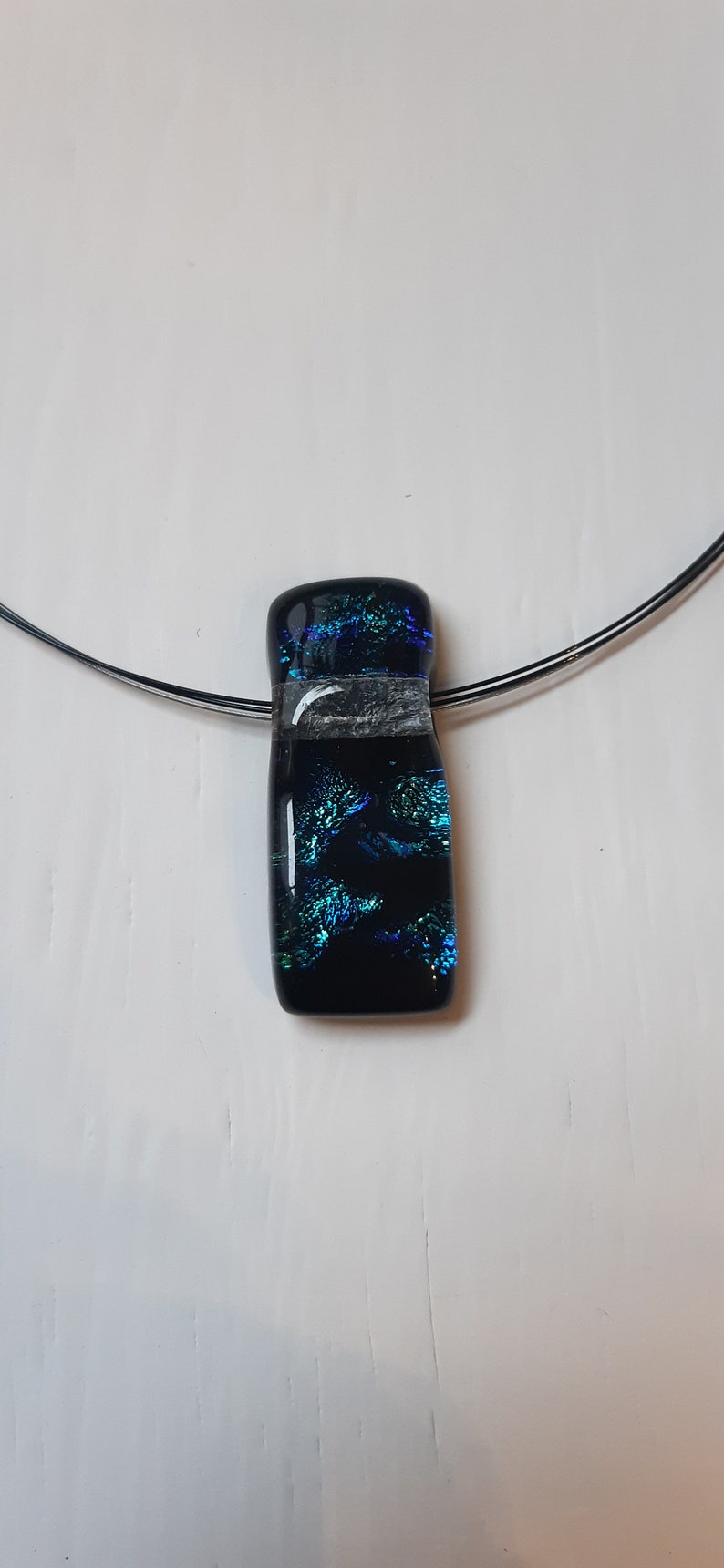 K&ouml;nnte beinhalten: Ein schwarzer Glasanh&auml;nger mit einem blauen und gr&uuml;nen, schillernden Muster h&auml;ngt an einer silbernen Kette.
