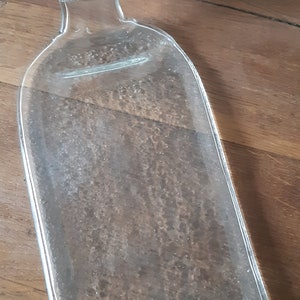 May include: A clear glass bottle shaped into a serving tray. The bottle has a textured surface and a rounded edge.