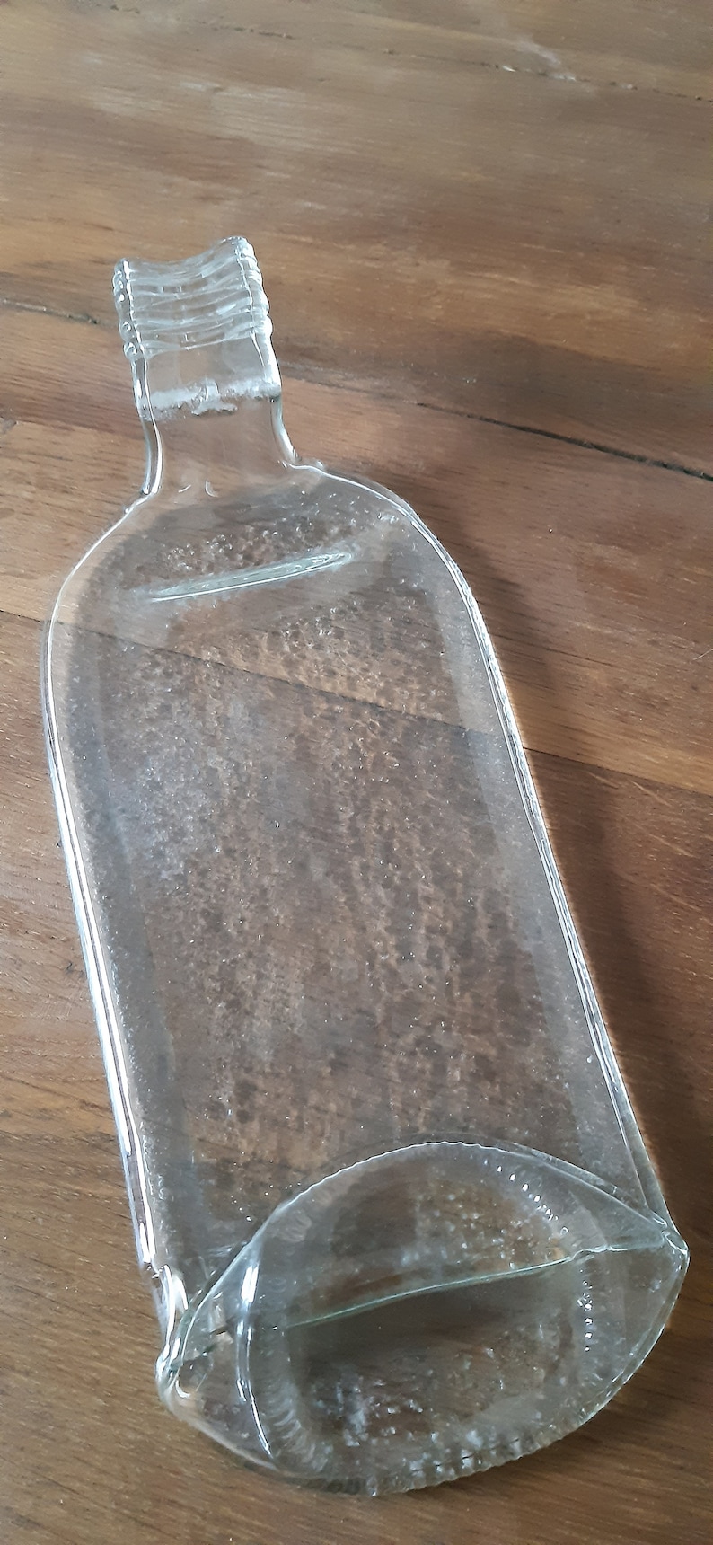 May include: A clear glass bottle shaped into a serving tray. The bottle has a textured surface and a rounded edge.