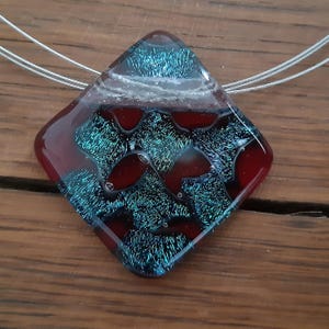 May include: A red and teal glass pendant with a diamond shape and a silver chain.