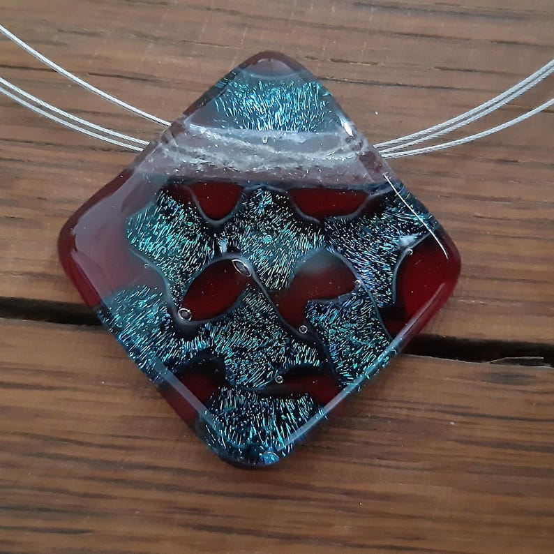 May include: A red and teal glass pendant with a diamond shape and a silver chain.