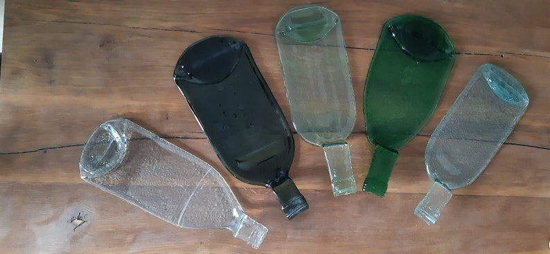 May include: Five glass serving trays made from recycled wine bottles. The trays are in various colors, including clear, green, and black.