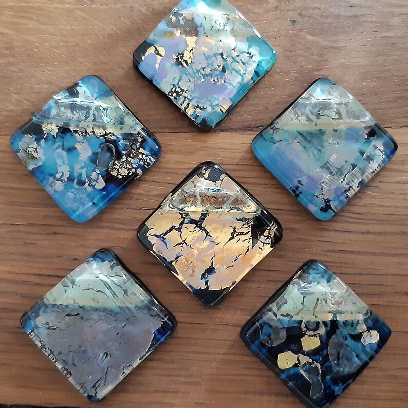 May include: Six diamond-shaped glass tiles with a blue, gold, and black abstract design. The tiles have a glossy finish and are perfect for adding a touch of color and texture to any space.