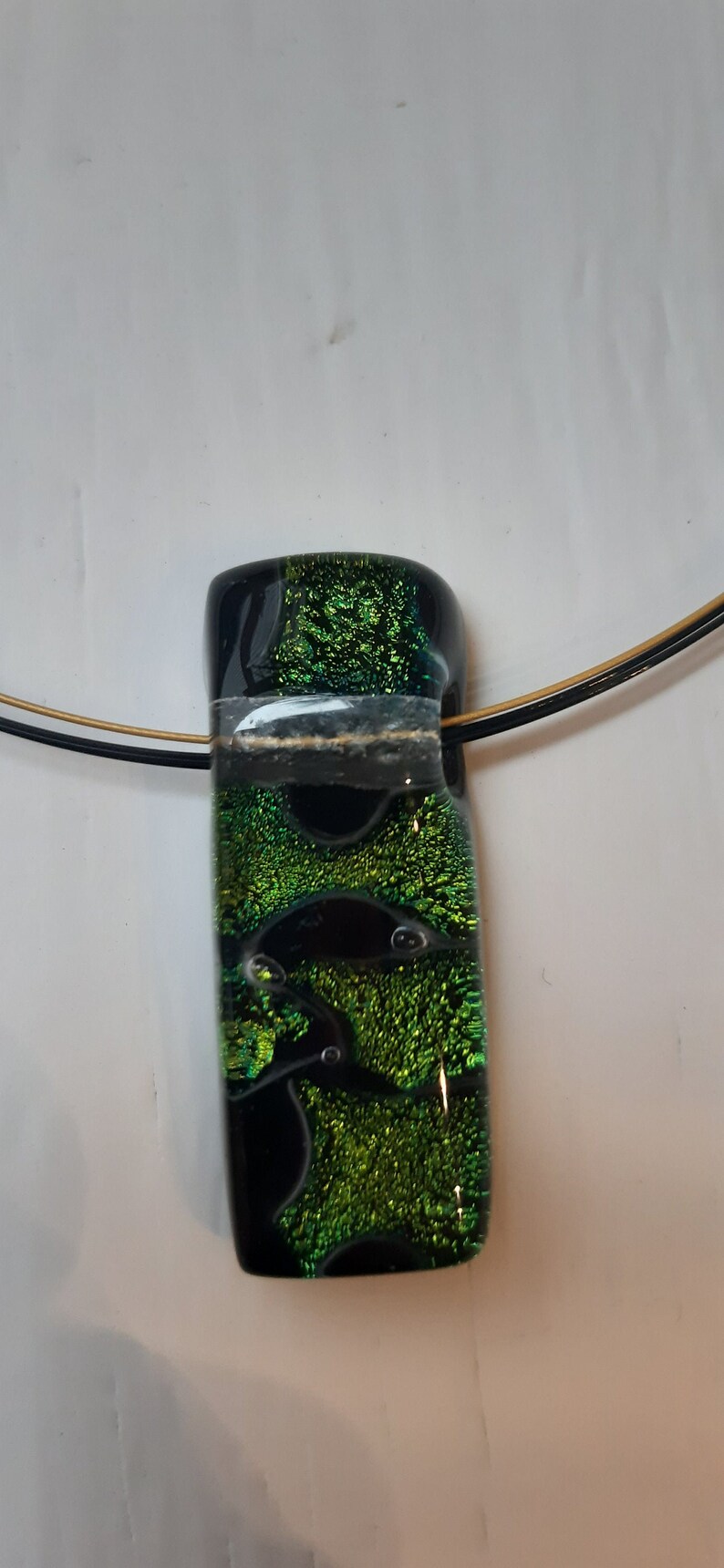 K&ouml;nnte beinhalten: Ein schwarzer und gr&uuml;ner Glasanh&auml;nger mit einer goldenen und schwarzen Schnur. Der Anh&auml;nger hat eine glitzernde, irisierende Oberfl&auml;che.