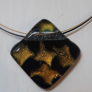 May include: A black and gold glass pendant with a geometric shape and a gold and green pattern. The pendant is hanging from a black and gold chain.