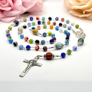May include: A colorful rosary with glass beads in various colors, including blue, green, yellow, and red. The rosary features a silver crucifix with a detailed depiction of Jesus. The beads are strung on a silver chain.