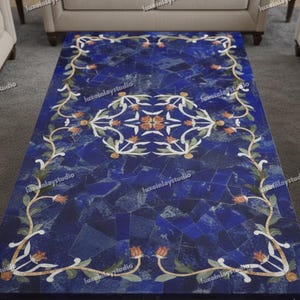 May include: Rectangular blue stone table with a floral design. The table's surface is a mosaic of blue pieces, with a white and orange floral border and central design. The table is surrounded by beige furniture.