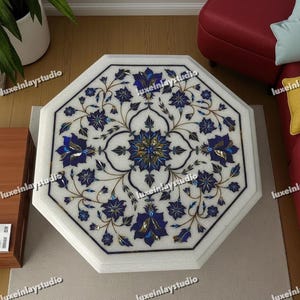 Puede incluir: Mesa octogonal de mármol blanco con diseño floral incrustado. El intrincado patrón presenta detalles en azul y dorado, creando una superficie decorativa. Una pieza de mobiliario única.