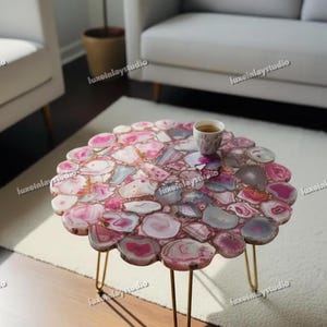 May include: A circular coffee table featuring a mosaic top made from pink and white agate slices. The table has a gold metal frame with three slender legs. A cup of coffee sits on the table.