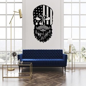 May include: A black and white wall decal featuring a skull design with an American flag pattern on the head. The skull has a detailed mustache and a full beard. The decal is mounted on a white wall above a blue sofa.