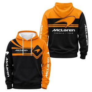 Könnte beinhalten: Ein schwarz-oranger Kapuzenpullover mit dem McLaren Formula 1 Team Logo auf der Brust und dem Rücken. Die Ärmel zeigen den Schriftzug McLaren in weißer Farbe, und die Kapuze hat weiße Kordelzüge sowie ein weißes Innenfutter.