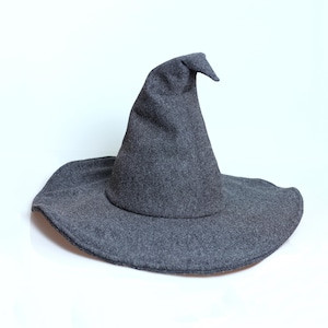 Puede incluir: Un sombrero de bruja gris con ala ancha y copa puntiaguda. El sombrero está hecho de un material suave, similar al fieltro, adecuado para Halloween o fiestas de disfraces.