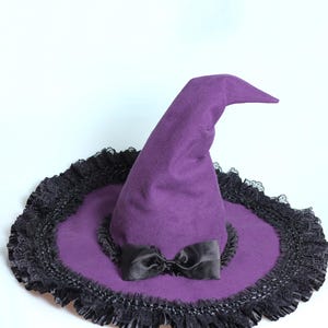 May include: A purple witch hat with a black bow and a wide brim. The brim is trimmed with black lace. The hat is made of a soft fabric and is suitable for Halloween or costume parties.