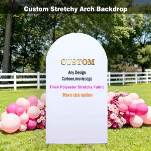 May include: A white, arched backdrop with gold text that reads "CUSTOM" and additional text below. The backdrop is made of thick, stretchy fabric and is supported by a wooden frame. Pink balloons and flowers decorate the base.